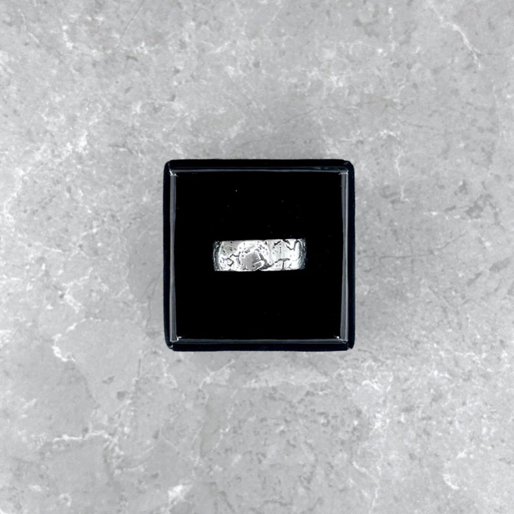 Der silberne Mancino "Broken" Ring stilvoll präsentiert in einer geöffneten schwarzen Schmuckbox auf einem hellgrauen Steinuntergrund.