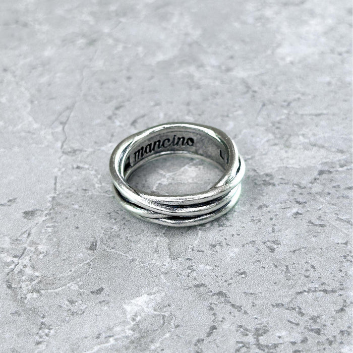 Nahaufnahme des Mancino "Filo Avvolto" Rings aus 925 Sterling Silber mit dynamischem, gewickeltem Faden-Design und graviertem Logo auf der glatten Innenseite, liegend auf einem hellgrauen Steinuntergrund.