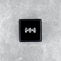 Der silberne Mancino "Giglio" Ring mit markantem Fleur-de-Lis-Muster, stilvoll präsentiert in einer geöffneten schwarzen Schmuckbox auf einem hellgrauen Steinuntergrund.