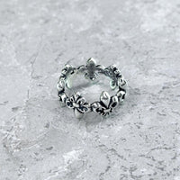 Nahaufnahme des Mancino "Giglio" Rings aus 925 Sterling Silber mit umlaufendem, plastischem Lilien-Motiv im Vintage-Finish, liegend auf einem hellgrauen Steinuntergrund.