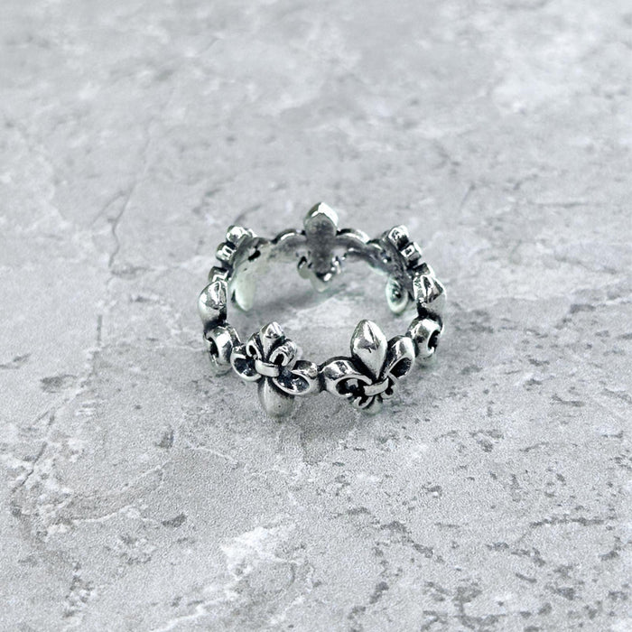 Nahaufnahme des Mancino "Giglio" Rings aus 925 Sterling Silber mit umlaufendem, plastischem Lilien-Motiv im Vintage-Finish, liegend auf einem hellgrauen Steinuntergrund.