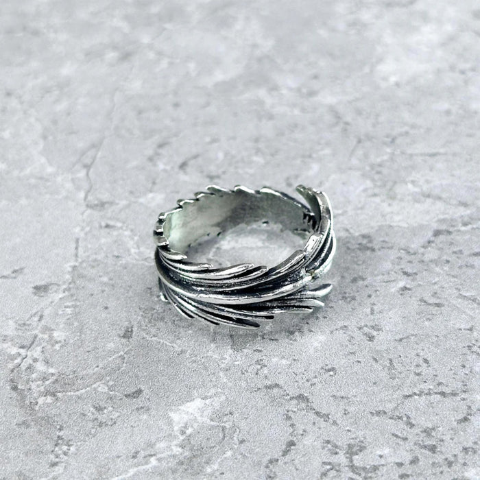 Nahaufnahme des Mancino "Piuma" Rings aus 925 Sterling Silber. Das detaillierte, plastische Feder-Motiv legt sich im Vintage-Finish um den Ring, freigestellt auf einem hellgrauen Steinuntergrund.