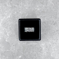 Der silberne Mancino "Piuma" Ring mit markantem Feder-Design, stilvoll präsentiert in einer geöffneten schwarzen Schmuckbox auf einem hellgrauen Steinuntergrund.