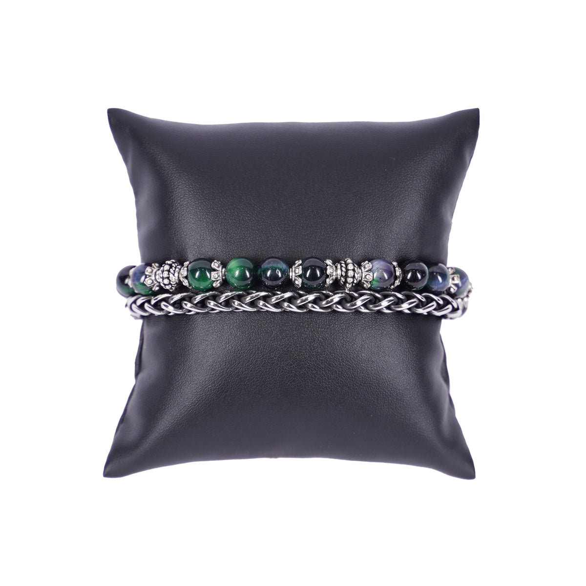 Zweilagiges Herrenarmband von Mancino aus einer silbernen Edelstahlkette und einer Perlenkette mit großen 8mm Steinen in Grün, Blau und Schwarz auf einem schwarzen Kissen.