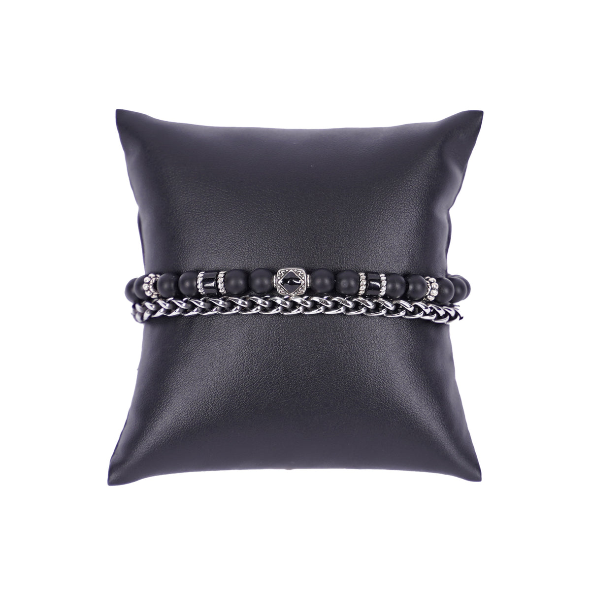 Zweilagiges Herrenarmband von Mancino aus einer silbernen Edelstahlkette und einer Perlenkette mit 6mm großen schwarzen und dunklen Natursteinen auf einem schwarzen Kissen.