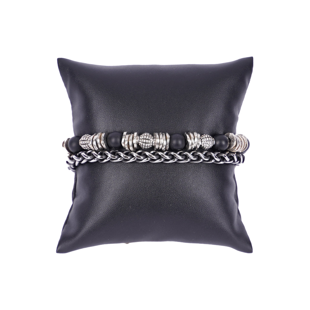 Zweilagiges Herrenarmband von Mancino aus silberner Edelstahlkette und einer Perlenkette mit großen 8mm matt-schwarzen Steinen und verzierten Silber-Elementen auf einem schwarzen Kissen.