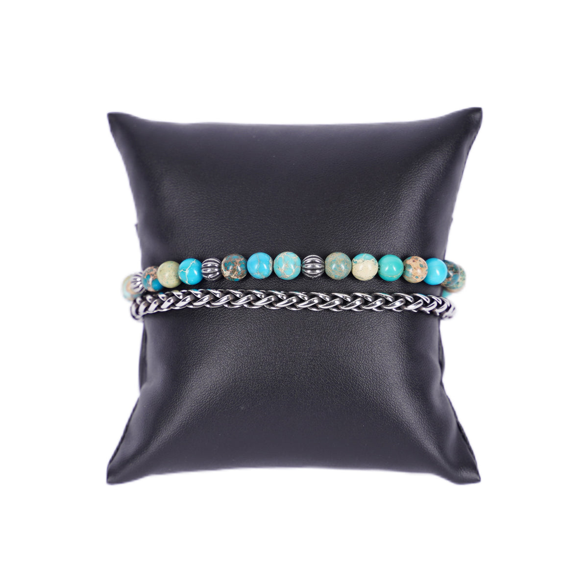Zweireihiges Mancino Armband "Due Giri", elegant präsentiert auf einem schwarzen Kissen. Eine Reihe besteht aus einer geflochtenen Edelstahlkette, die zweite aus 6mm Natursteinen in leuchtendem Türkis mit erdigen Einschlüssen und antiksibernen Metalldetails.