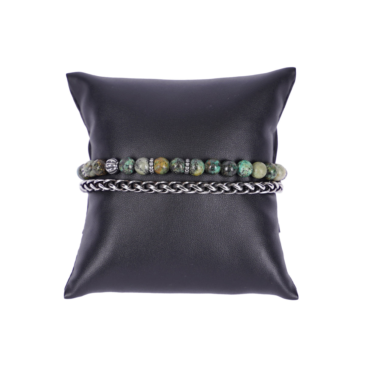 Zweireihiges Mancino Armband "Due Giri", elegant präsentiert auf einem schwarzen Kissen. Eine Reihe besteht aus einer geflochtenen Edelstahlkette, die zweite aus 6mm Natursteinen in gedecktem Grün mit braunen Einschlüssen und antiksibernen Metalldetails.