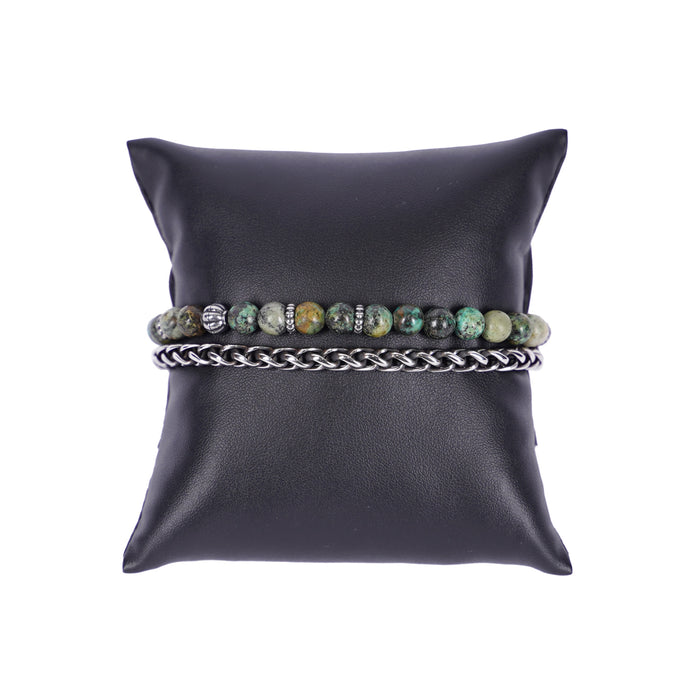 Zweireihiges Mancino Armband "Due Giri", elegant präsentiert auf einem schwarzen Kissen. Eine Reihe besteht aus einer geflochtenen Edelstahlkette, die zweite aus 6mm Natursteinen in gedecktem Grün mit braunen Einschlüssen und antiksibernen Metalldetails.