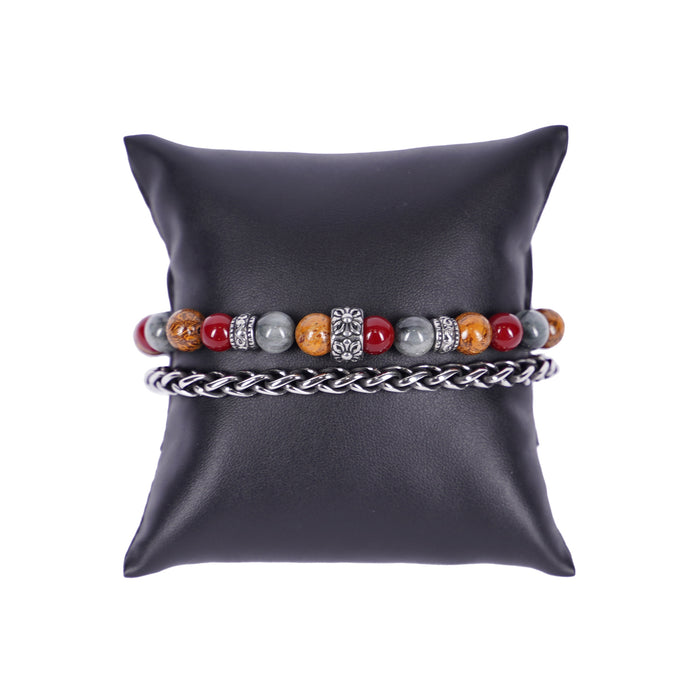 Zweireihiges Mancino Armband "Due Giri", elegant präsentiert auf einem schwarzen Kissen. Eine Reihe besteht aus einer geflochtenen Edelstahlkette, die zweite aus massiven 8mm Natursteinen in Tiefrot, Braun und Grau mit einem kunstvollen antiksilbernen Mittelstück.