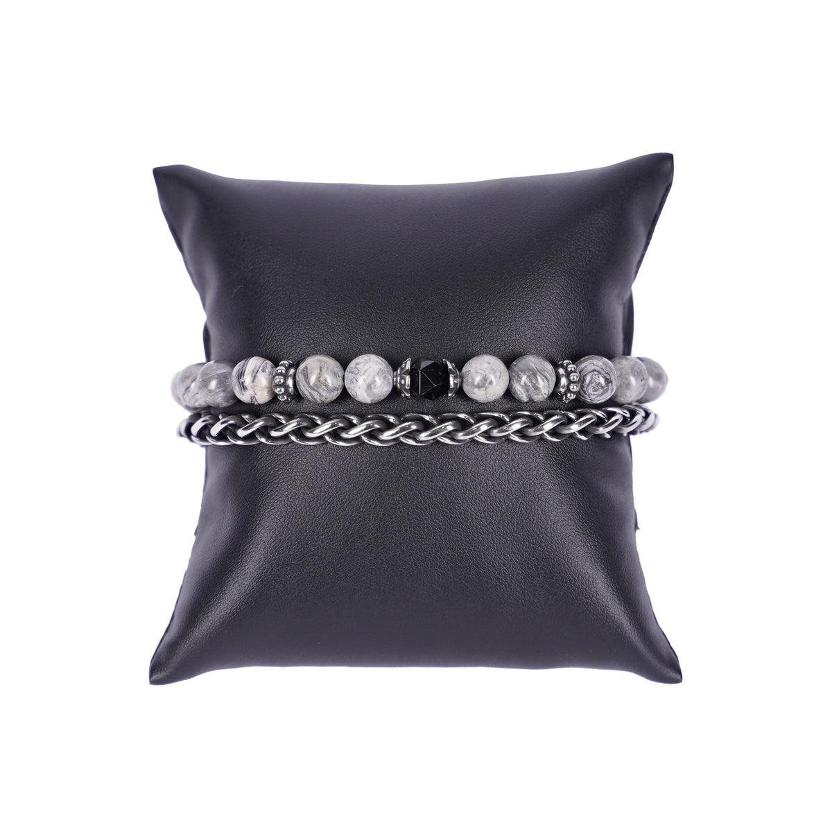 Zweireihiges Mancino Armband "Due Giri", elegant präsentiert auf einem schwarzen Kissen. Eine Reihe besteht aus einer geflochtenen Edelstahlkette, die zweite aus massiven 8mm Natursteinen in Grau-Weiß marmoriert mit einem schwarz facettierten Mittelstück und antiksilbernen Details.