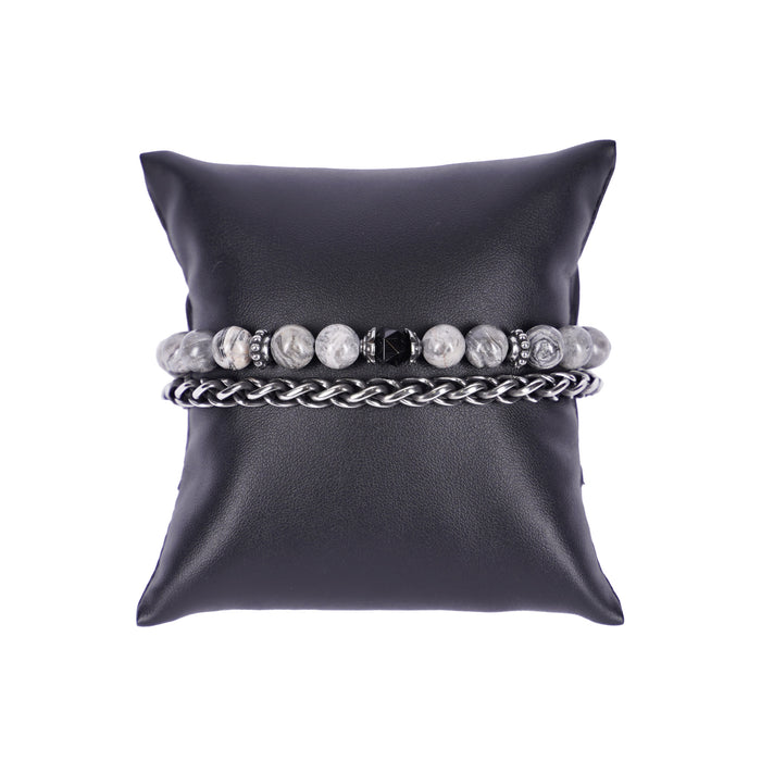 Zweireihiges Mancino Armband "Due Giri", elegant präsentiert auf einem schwarzen Kissen. Eine Reihe besteht aus einer geflochtenen Edelstahlkette, die zweite aus massiven 8mm Natursteinen in Grau-Weiß marmoriert mit einem schwarz facettierten Mittelstück und antiksilbernen Details.