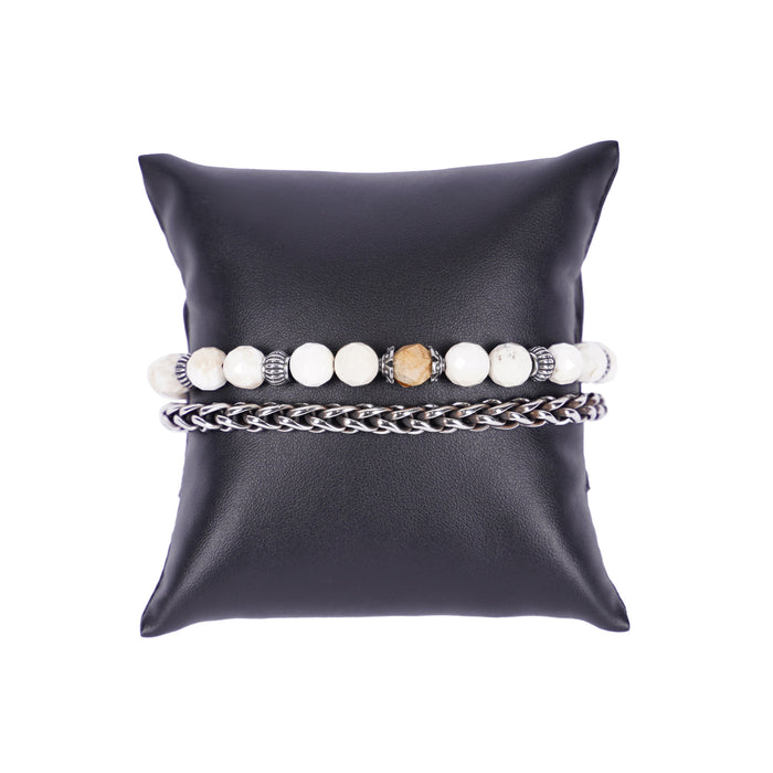 Zweireihiges Mancino Armband "Due Giri", elegant präsentiert auf einem schwarzen Kissen. Eine Reihe besteht aus einer geflochtenen Edelstahlkette, die zweite aus massiven 8mm Natursteinen in Weiß (facettiert geschliffen) mit einem sandfarbenen Mittelstück und antiksilbernen Details.