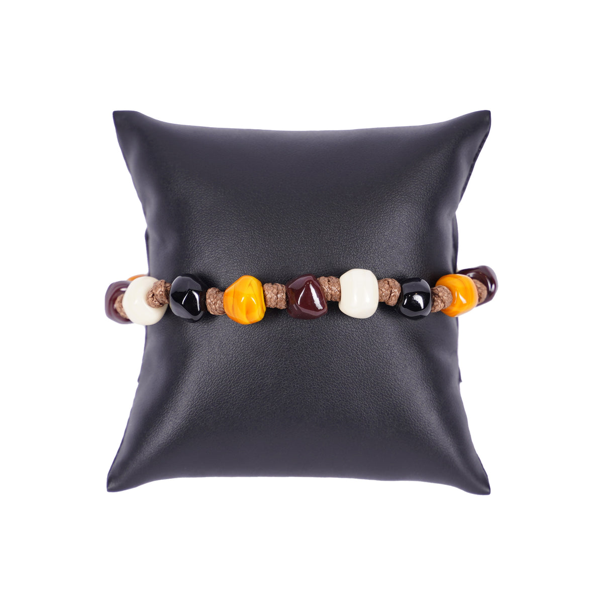 Herrenarmband von Mancino aus brauner geflochtener Kordel mit bunten Muranoglas-Perlen in Ocker, Weiß und Schwarz auf einem schwarzen Kissen.