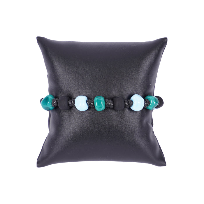 Herrenarmband von Mancino aus schwarzer geflochtener Kordel mit türkisfarbenen und hellblauen Muranoglas-Perlen auf einem schwarzen Kissen.