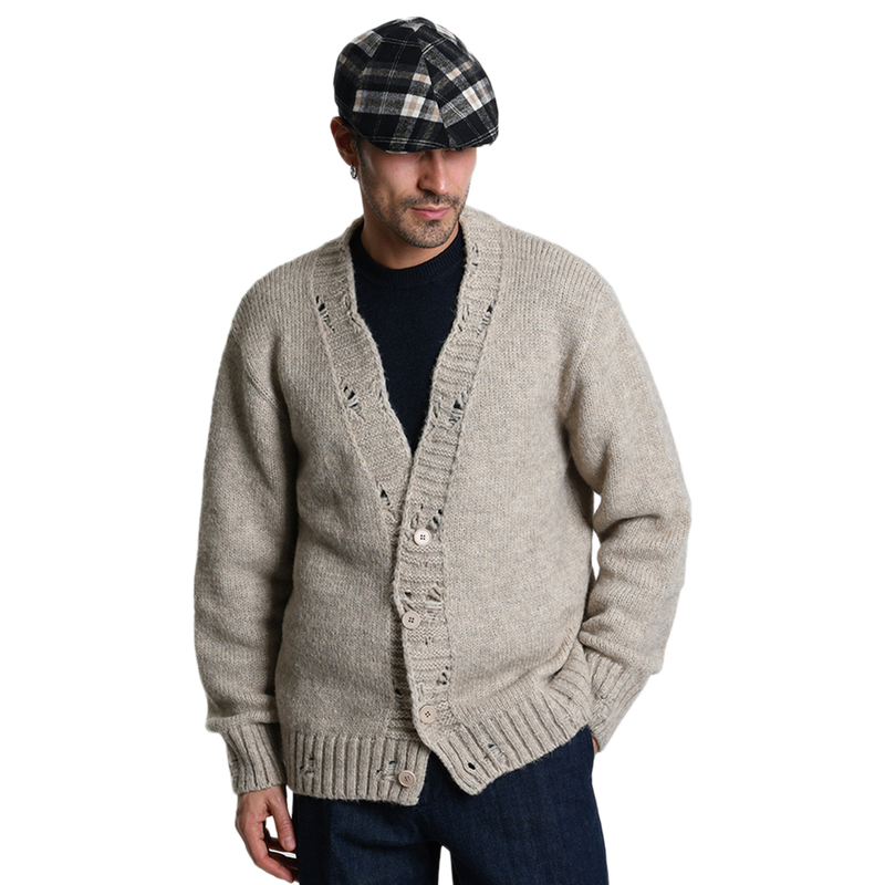 Lässiger Heritage-Look mit dem beigen Xagon Cardigan. Das Model kombiniert die grob gestrickte Jacke mit den gewollten Rissen (Rotture) stilvoll mit einer karierten Schiebermütze.