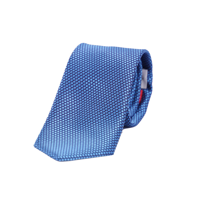 Klassisch geschnittene, elegant gerollte Seidenkrawatte von VP Italian Brand in Mittelblau mit feiner, punktförmiger Oberflächenstruktur auf weißem Hintergrund.