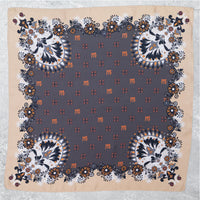 Flach ausgebreitetes Mancino Seiden-Foulard (100% Seide). Das Design zeigt ein dunkelgraues Zentrum mit orangefarbenen 'm'-Logos und eine aufwendige florale Paisley-Bordüre in Sand, und Orange.