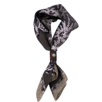 Geknotetes Mancino Seiden-Foulard "Tropical Green" (51x51 cm) mit Palmenmuster, fixiert durch ein braunes Leder-Bolo mit türkisfarbenem Naturstein, freigestellt auf weißem Hintergrund.