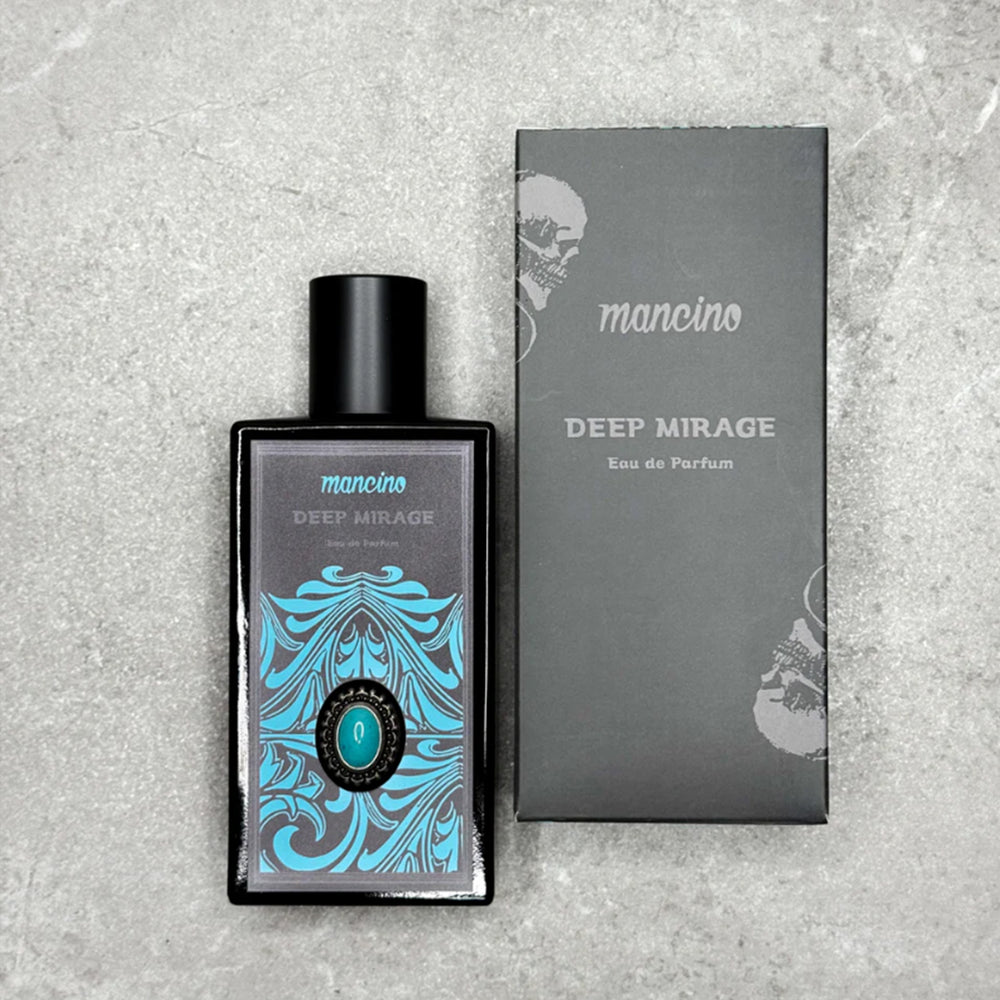 Draufsicht einer Produktfotografie des Mancino Deep Mirage Eau de Parfum neben seiner mattschwarzen Verpackung auf einer grau-strukturierten Steinfläche. Der Flakon zeigt das detaillierte Etikett mit hellblauen Akzenten und dem zentralen Türkis-Stein. Die Box ist mit dem silbernen Mancino-Schriftzug und einem dezenten Totenkopf-Motiv veredelt.