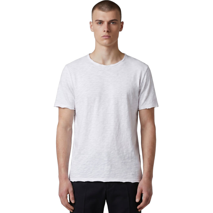 Frontansicht eines männlichen Models in einem weißen Slub-Cotton T-Shirt mit ungesäumten Raw-Edge-Abschlüssen und schwarzer Hose.