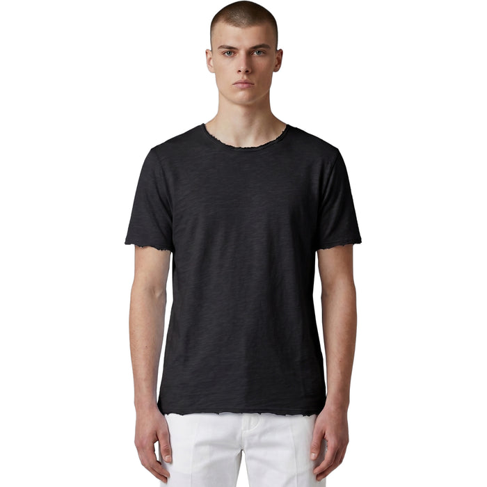 Frontansicht eines männlichen Models in einem schwarzen Slub-Cotton T-Shirt mit ungesäumten Raw-Edge-Abschlüssen und weißer Hose.