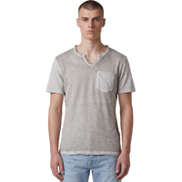 Frontansicht eines männlichen Models, das das beigefarbene T-Shirt mit V-Ausschnitt trägt. Deutlich erkennbar sind die strukturierte Slub-Baumwolle, die offenkantigen Raw-Edge-Details an Kragen, Ärmeln und Bund sowie die aufgesetzte Brusttasche. Das Shirt wird lässig zu einer hellblauen Jeans präsentiert.