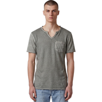 Frontansicht eines männlichen Models, das das salbeigrüne T-Shirt mit V-Ausschnitt trägt. Deutlich erkennbar sind die strukturierte Slub-Baumwolle, die offenkantigen Raw-Edge-Details an Kragen, Ärmeln und Bund sowie die aufgesetzte Brusttasche. Das Shirt wird lässig zu einer hellblauen Jeans.