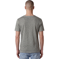 Rückansicht eines männlichen Models in dem salbeigrünen T-Shirt. Der Fokus liegt auf der feinen Melange-Struktur des Stoffes, dem lässigen Schnitt und dem leicht ausgefransten Raw-Edge-Saum am unteren Bund. Das Model trägt eine hellblaue Jeans.