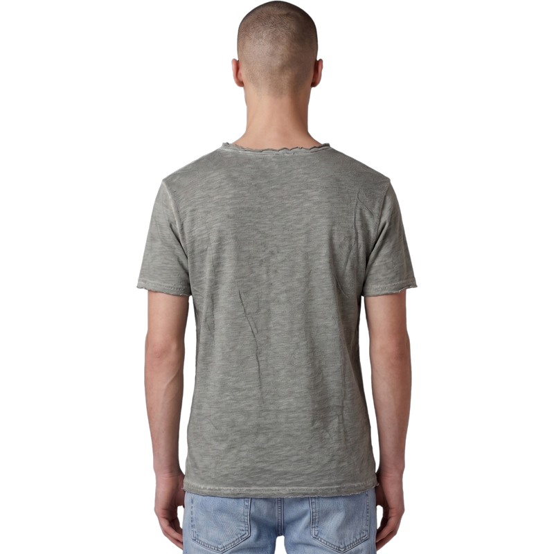 Rückansicht eines männlichen Models in dem salbeigrünen T-Shirt. Der Fokus liegt auf der feinen Melange-Struktur des Stoffes, dem lässigen Schnitt und dem leicht ausgefransten Raw-Edge-Saum am unteren Bund. Das Model trägt eine hellblaue Jeans.