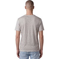 Rückansicht eines männlichen Models in dem beigefarbenen T-Shirt. Der Fokus liegt auf der feinen Melange-Struktur des Stoffes, dem lässigen Schnitt und dem leicht ausgefransten Raw-Edge-Saum am unteren Bund. Das Model trägt eine hellblaue Jeans.