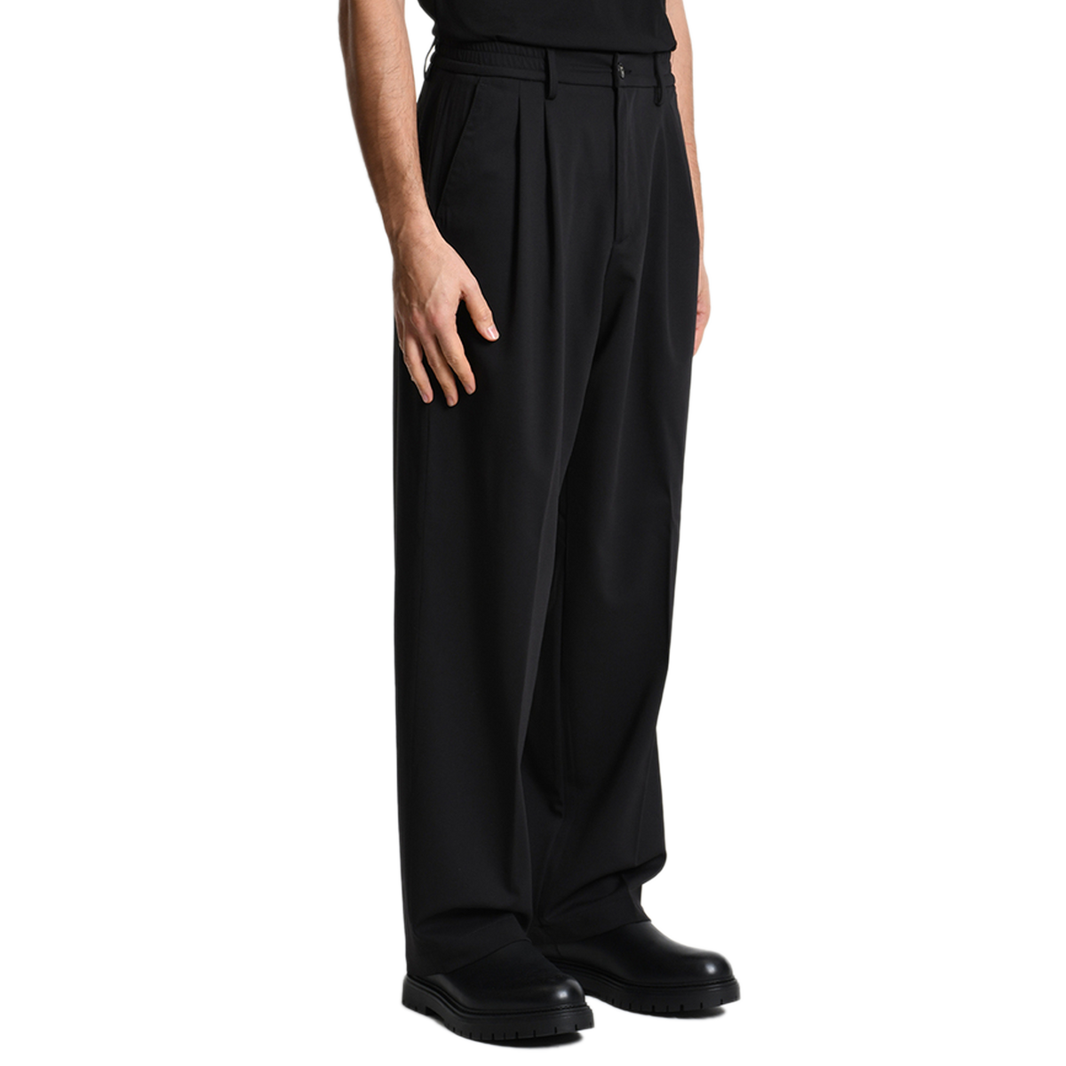 Seitliche Profilansicht der schwarzen Xagon Wide Fit Hose. Der fließende Fall des Stoffes und der lässige Schnitt kommen in Kombination mit schwarzen Leder-Boots perfekt zur Geltung.