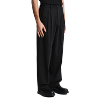 Seitliche Profilansicht der schwarzen Xagon Wide Fit Hose. Der fließende Fall des Stoffes und der lässige Schnitt kommen in Kombination mit schwarzen Leder-Boots perfekt zur Geltung.